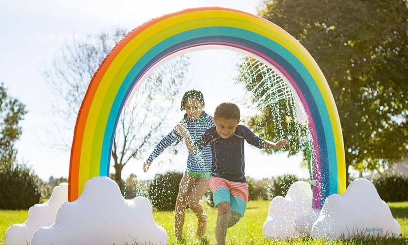 Kids run through rainbow sprinkler